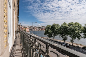 A balcony with a railing overlooking a river, a cityscape in the distance, and a clear sky.