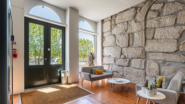 Un vestíbulo moderno con una pared de piedra, un sofá gris, una mesa de centro y una puerta con vistas al exterior.