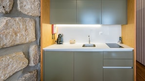 Una cocina compacta con pared de piedra, una cafetera, un lavabo y una pequeña cesta.