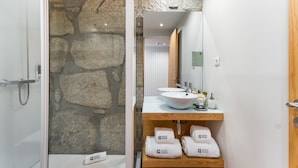Un baño con pared de piedra, ducha, lavamanos con espejo y repisa con toallas etiquetadas 'GUEST READY'.