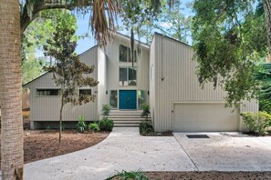 Um edifício de dois andares com porta azul, garagem e pequeno alpendre com degraus que levam à entrada.