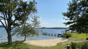 Une vue sur le lac, avec une jetée en bois s’avançant dans l’eau, entourée de zones herbeuses et d’arbres.