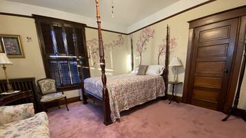 A bedroom with a four-poster bed, a floral-patterned sofa, a wooden chair, and a wooden door.