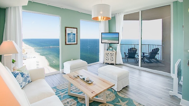 A spacious balcony with a view of the ocean, furnished with white sofas, a coffee table, and chairs.