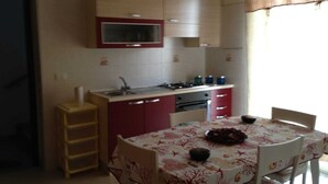 Une cuisine compacte équipée d’un évier, d’une cuisinière et de placards. On y trouve une table à manger avec des chaises et une nappe décorative.