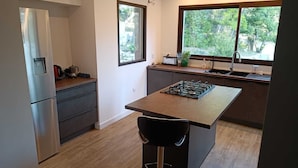 A modern kitchen with a central island, stainless steel appliances, and large windows offering a view of greenery. - Nature in Aix (Venelles)