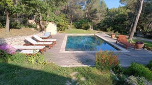 A rectangular swimming pool with a wooden deck surrounding it, lounge chairs, and potted plants. - Nature in Aix (Venelles)