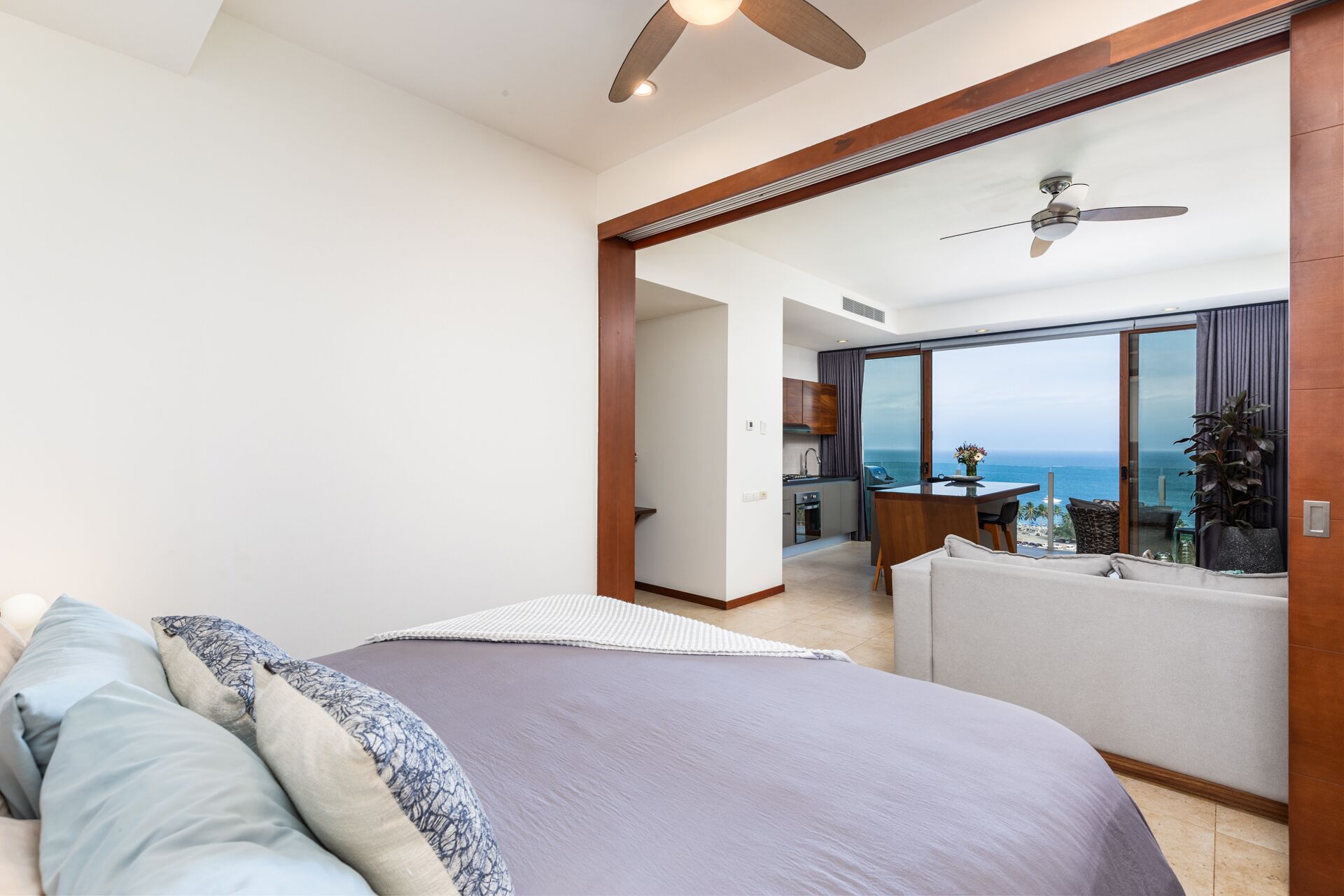 A modern hotel room with a large bed, a balcony with a view of the sea, and a separate dining area.