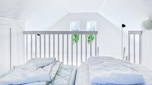Un dormitorio con dos camas, paredes blancas, techo inclinado y dos ventanas.