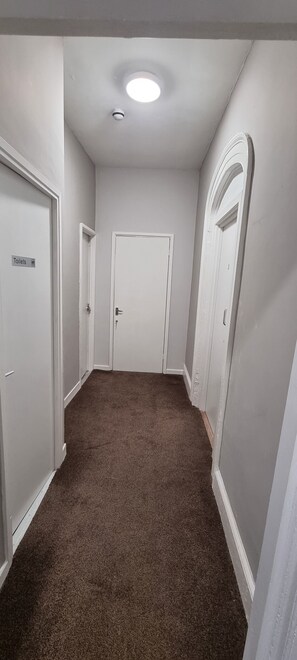 A hallway with carpeted flooring, white walls, and doors, including a sign indicating a toilet. - City Express (Plymouth)