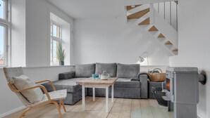 En moderne stue med en grå hjørnesofa, et træsofabord, en fletkurv og en grå pejs.