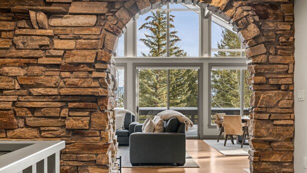 Un arco de piedra que da acceso a una sala de estar con un ventanal grande, un sofá y una silla.