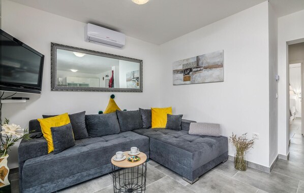 Ein modernes Wohnzimmer mit einem grauen Ecksofa, einem Flachbildfernseher, einem großen Spiegel und einem Gemälde an der Wand.