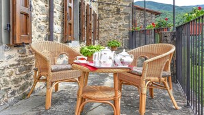 Un tavolo in vimini apparecchiato con un set da tè su un patio con lastre di pietra, adiacente a un edificio in pietra con persiane in legno.