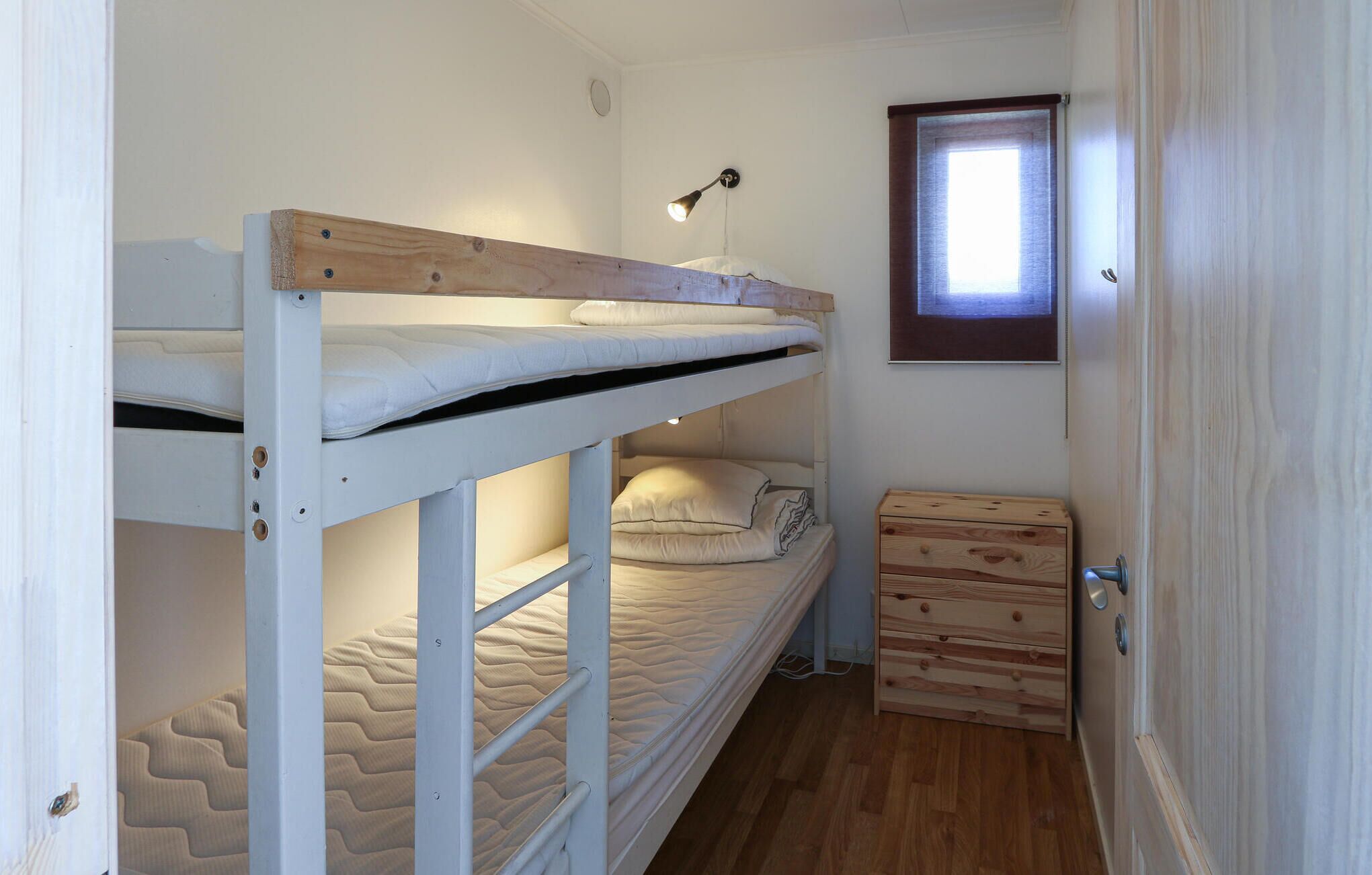 Een slaapkamer met een stapelbed, een raam, een bureau en een lamp.