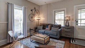 Een woonkamer met een bank, salontafel, stoel, lamp en een fiets bevestigd aan de muur.