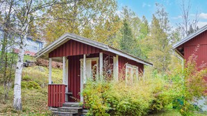 Eine kleine, rote Holzhütte mit Veranda, umgeben von Bäumen und Sträuchern.