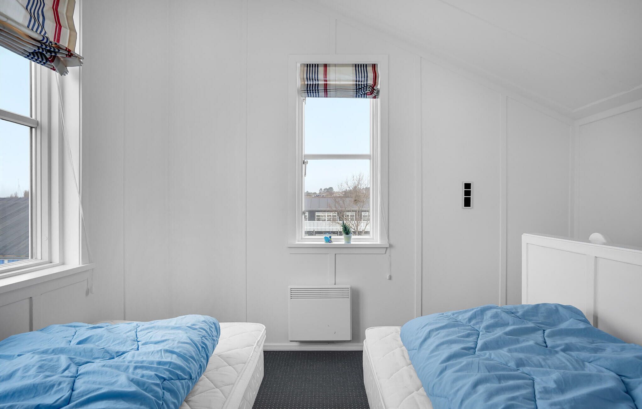 A bedroom with two beds, a window with a view, a radiator, and a small plant on the windowsill.