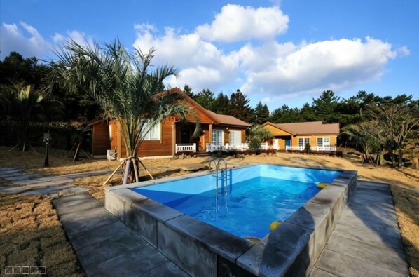 A two-story house with a swimming pool, surrounded by a wooden fence and palm trees. - Garten In AEWOL (Jeju City)
