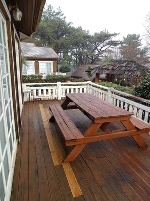 A wooden deck with a picnic table, white railings, and a house in the background. - Garten In AEWOL (Jeju City)