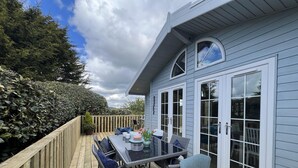 Une terrasse avec une table et des chaises, un pot de fleurs et une vue sur une maison bleue aux grandes fenêtres.