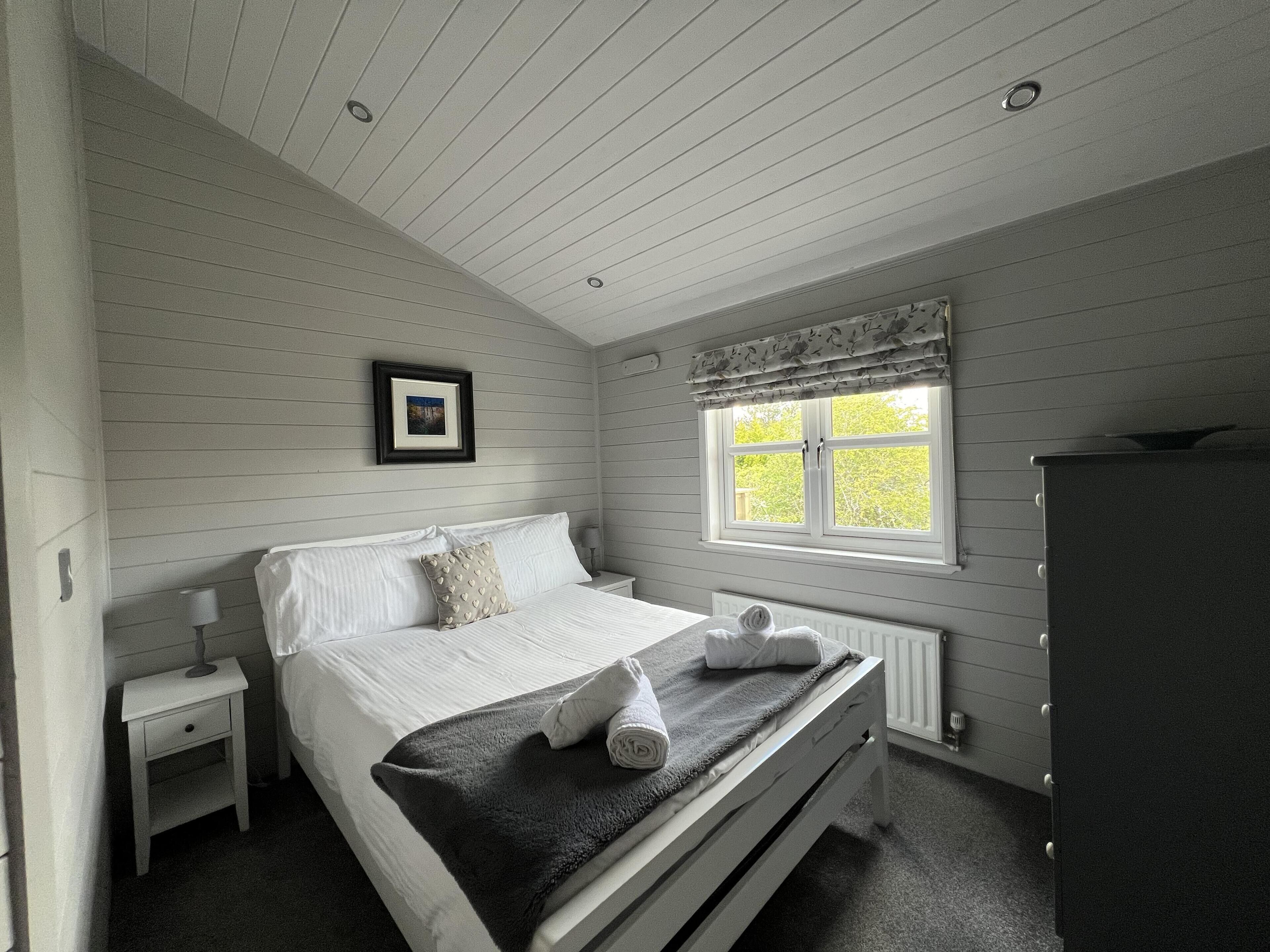 Ein Schlafzimmer mit Bett, Nachttisch, Kommode, Fenster und einem gerahmten Bild an der Wand.