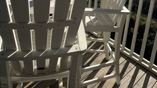 A covered deck with white Adirondack chairs overlooking a beach. - Beachfront Condo with Amazing Ocean Views (Pine Knoll Shores)
