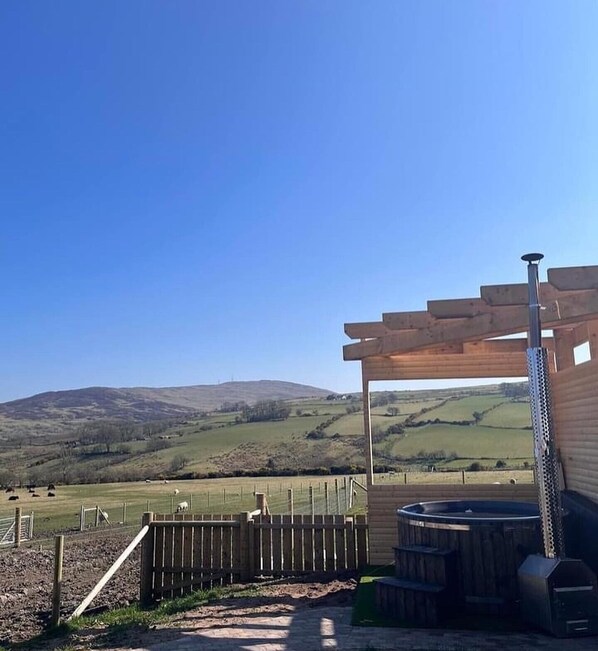 A rustic outdoor area with a wooden pergola, a hot tub, and a view of rolling hills. - Dan’s Wee Cottage - Slieve Croob, Dromara (hot tub included in price) (Dromara)