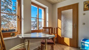 A dining area with a table and chairs, a window with a view of snow-covered trees, a door with a frosted glass panel, and a blue trash bin labeled "BIOABFALL". - Awesome home in Kranichfeld with WiFi (Kranichfeld)
