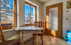 A dining area with a table and chairs, a window with a view of snow-covered trees, a door with a frosted glass panel, and a blue trash bin labeled "BIOABFALL". - Awesome home in Kranichfeld with WiFi (Kranichfeld)