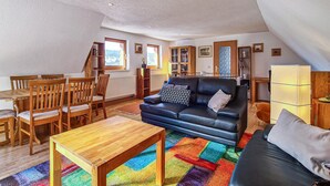 A cozy living room with a black leather sofa, wooden dining table, and chairs. There is a colorful rug on the floor, and a window provides natural light. - Awesome home in Kranichfeld with WiFi (Kranichfeld)