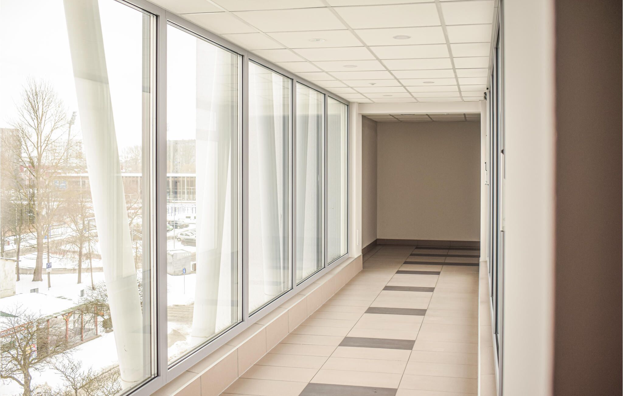 A corridor with large windows, tiled floor, and a view of a snowy outdoor area.