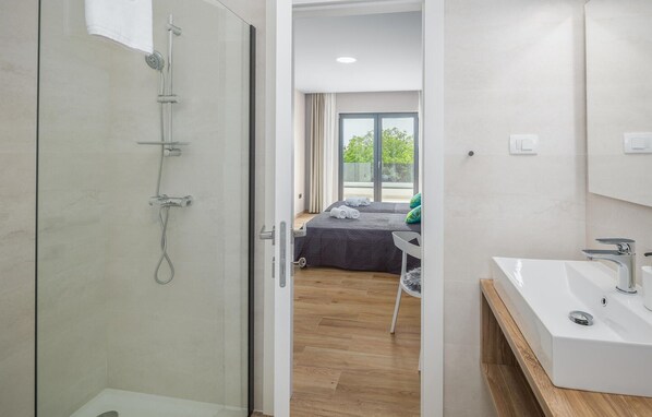 Une salle de bain moderne avec une douche à l’italienne en verre, un lavabo blanc et un lit donnant sur l’extérieur.