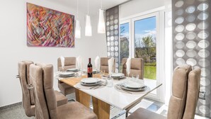 A dining area with a table set for six, six beige chairs, a large abstract painting, and a view of a garden through a glass door. - Gorgeous home in Kastav with WiFi (Kastav)
