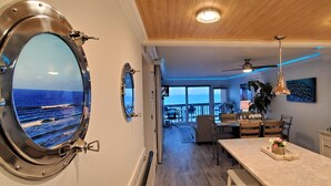 A modern kitchen with a large island, a dining area with chairs, and a view of the ocean through a porthole window.