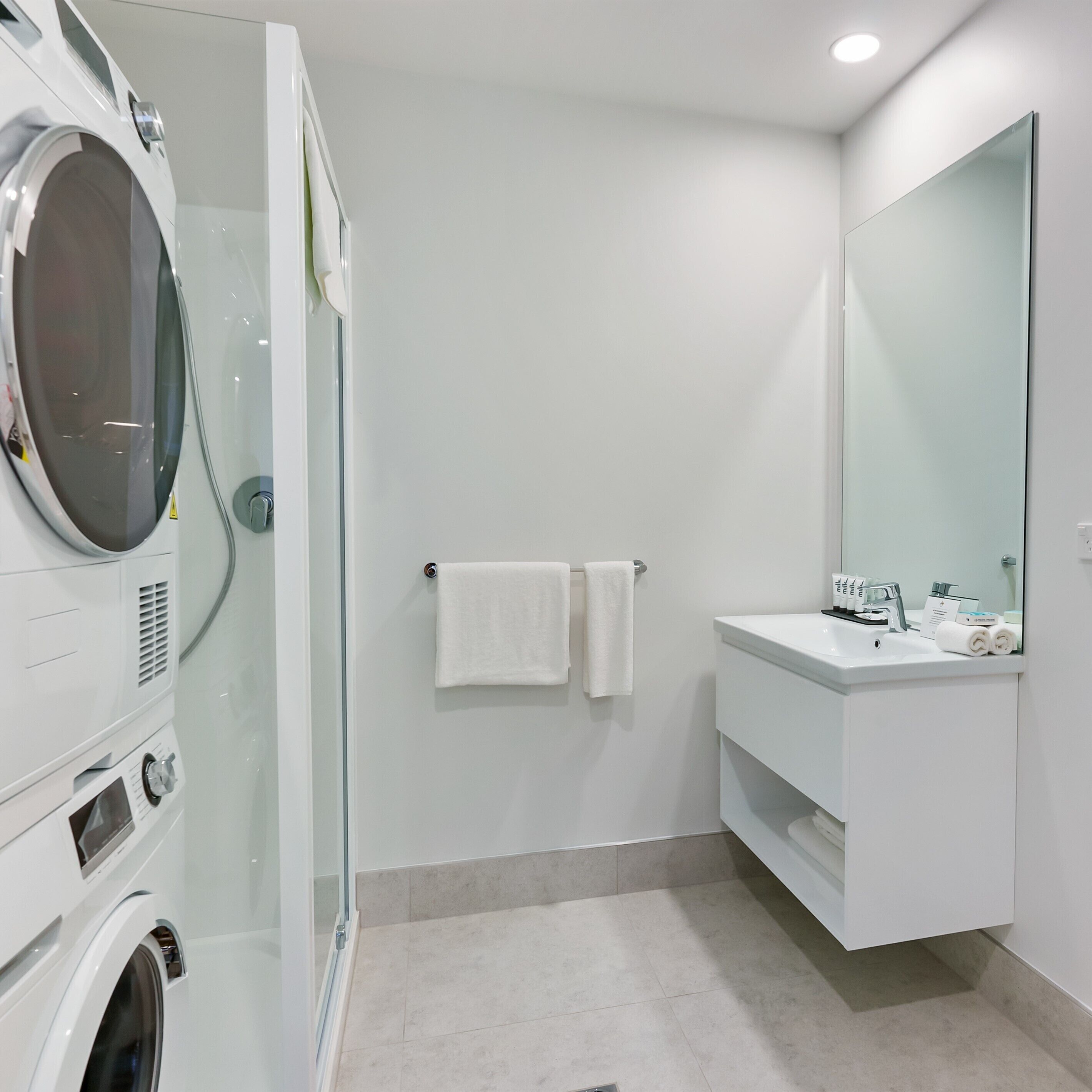 A modern bathroom with a glass-enclosed shower, a white sink with a mirror, and a built-in washing machine.