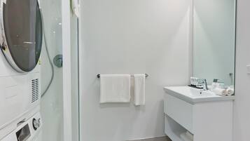 A modern bathroom with a glass-enclosed shower, a white sink with a mirror, and a built-in washing machine.