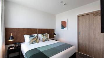 Habitación de hotel con una cama grande, cabecera de madera, mesita de noche con lámpara y un armario de madera.
