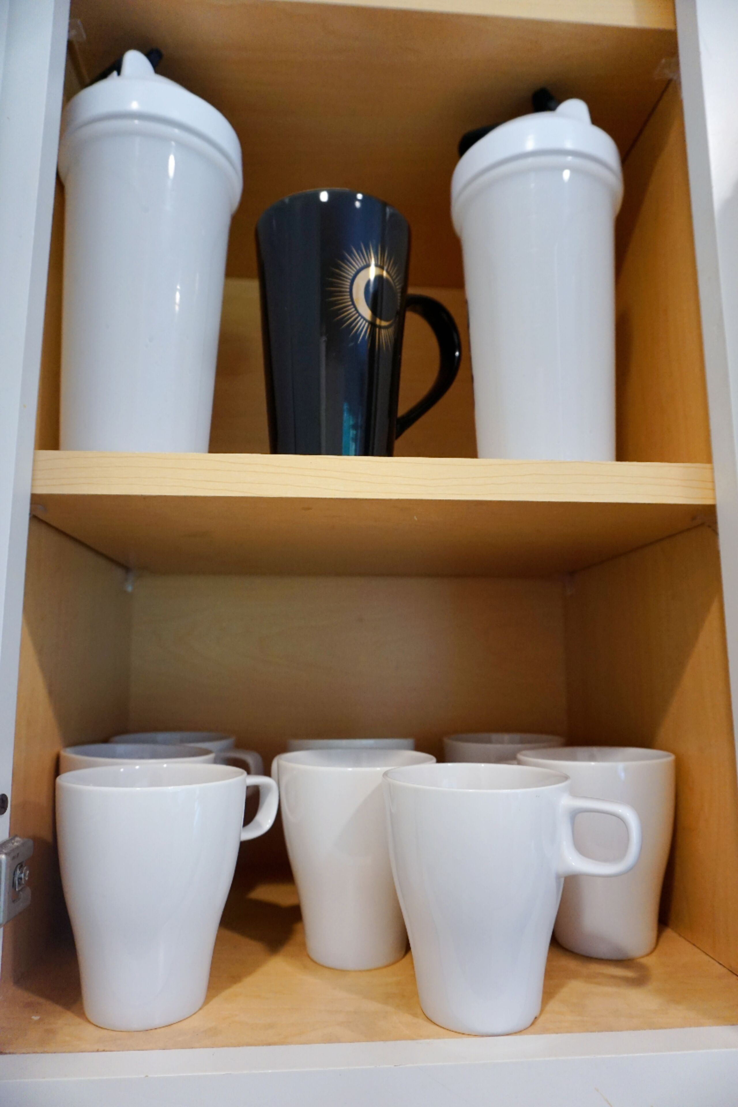A shelf with white and one black mug, and a white container.