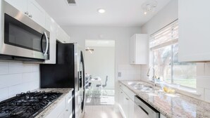 A modern kitchen with white cabinets, a stainless steel range, a black refrigerator, and a granite countertop.