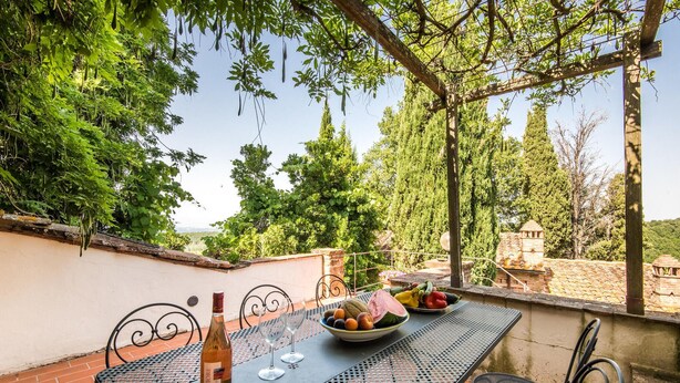 An outdoor patio with a table set for two, a bottle of wine, and a bowl of fruit. - Gorgeous apartment in Montaione (Montaione)