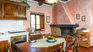 A rustic kitchen with wooden cabinets, a stone fireplace, and a dining table set with fruit. - Gorgeous apartment in Montaione (Montaione)