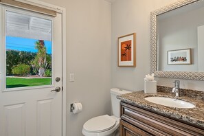 Une salle de bain équipée de toilettes, d’un lavabo et d’une fenêtre donnant sur un espace verdoyant.