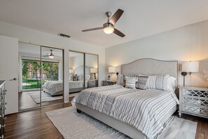 Une chambre dotée d’un grand lit, d’un ventilateur de plafond, de lampes de chevet, d’une table de chevet et donnant sur un espace extérieur grâce à une porte vitrée.