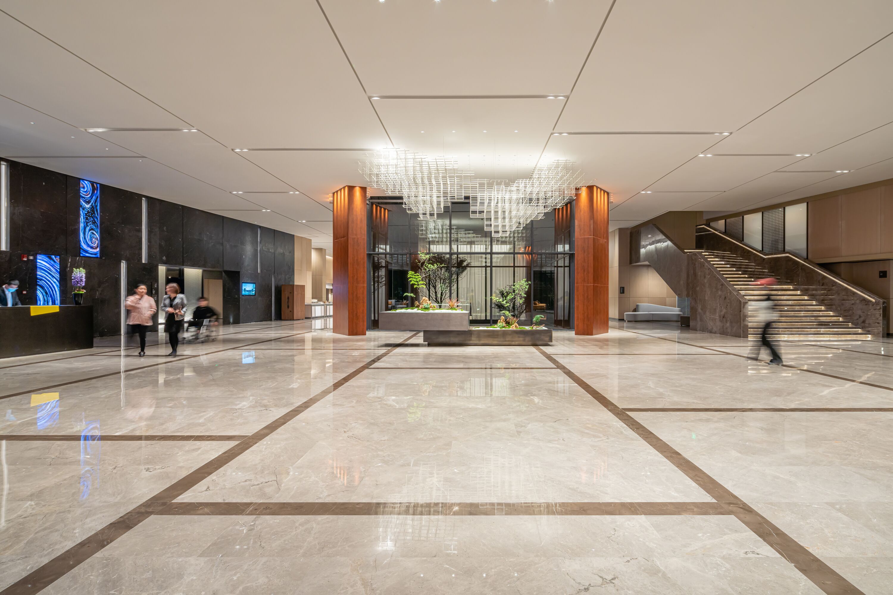 Eine geräumige Lobby mit einem zentralen Blumentopf, einer Treppe und einem Empfangsbereich.