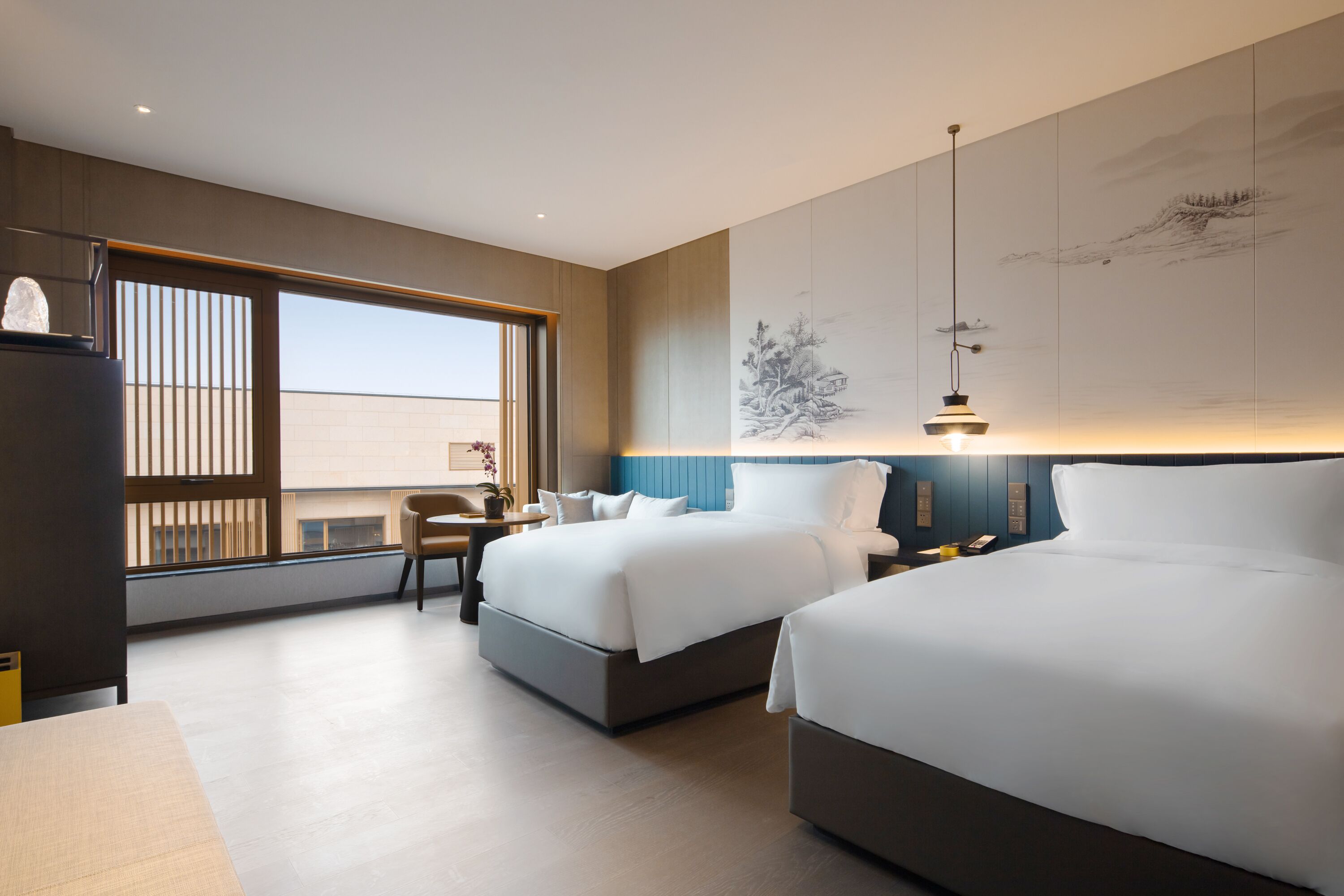 A modern hotel room with two beds, a desk, and a large window.