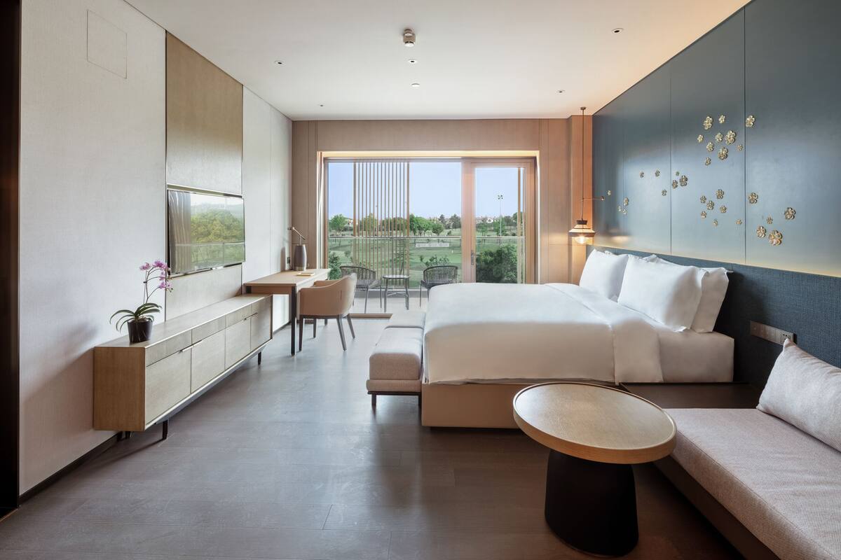 Una habitación de hotel moderna con una cama grande, un escritorio, una silla y vistas al exterior.