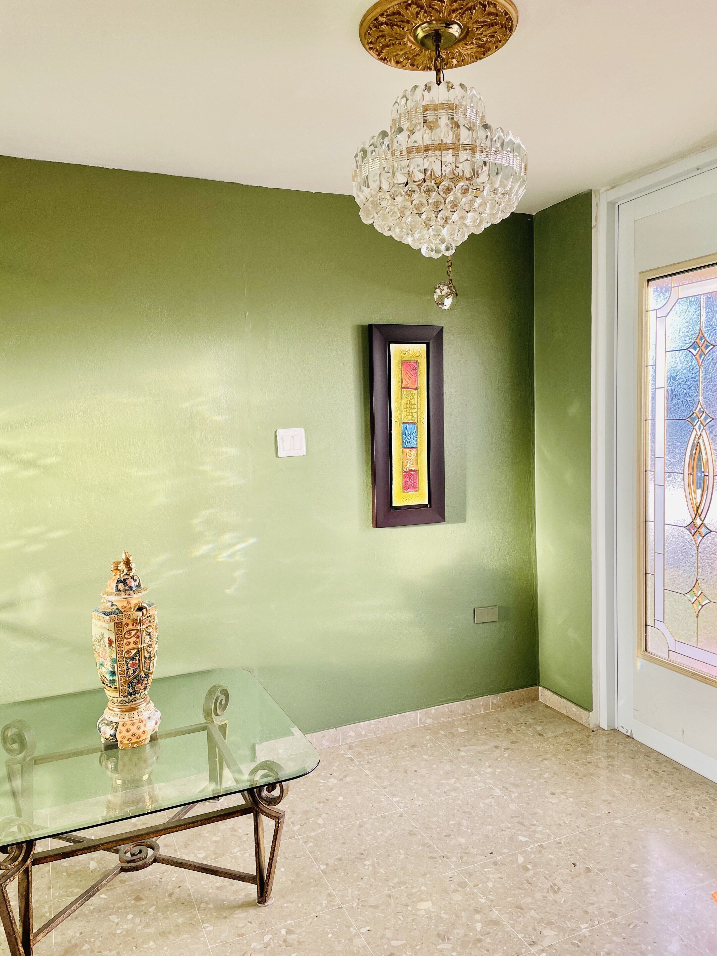 A dining area with a glass table, a decorative urn, a chandelier, and a framed picture on the wall.