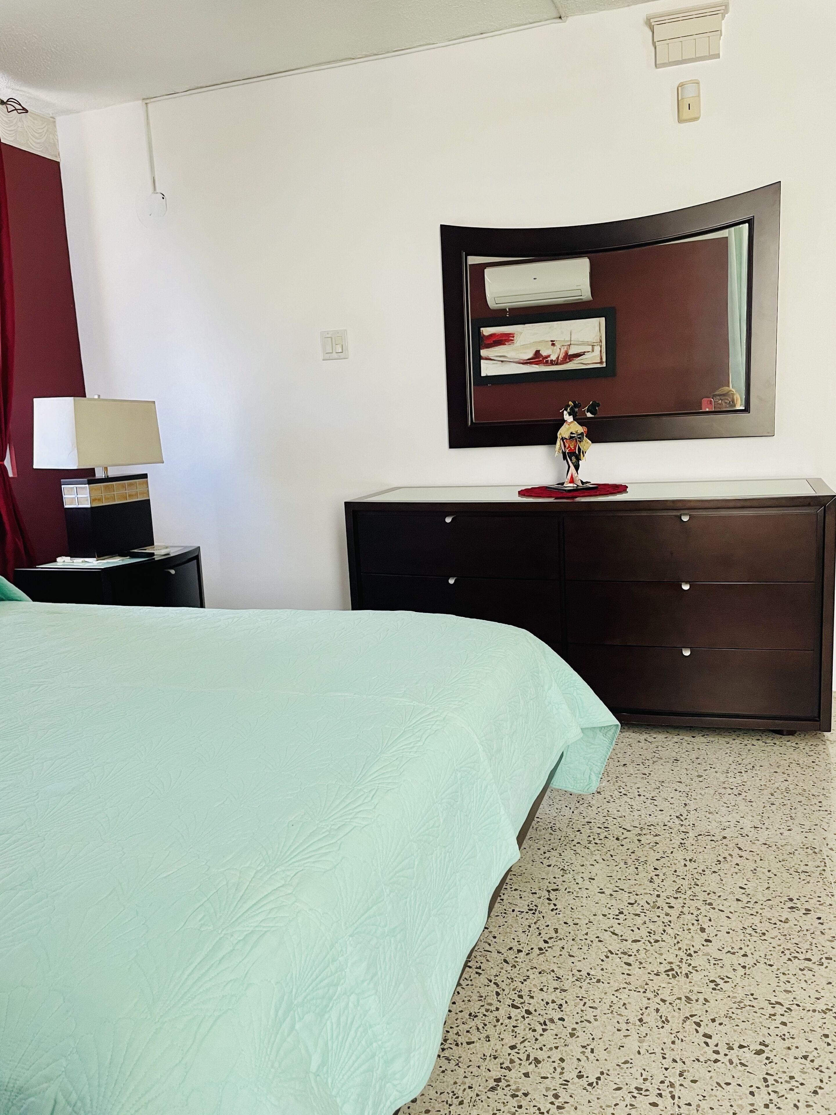 Une chambre d’hôtel avec un lit, une commode, une lampe et un miroir au mur.