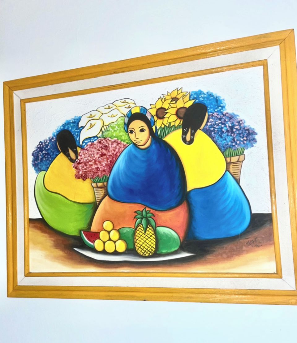 A framed painting of three figures with fruits and flowers.